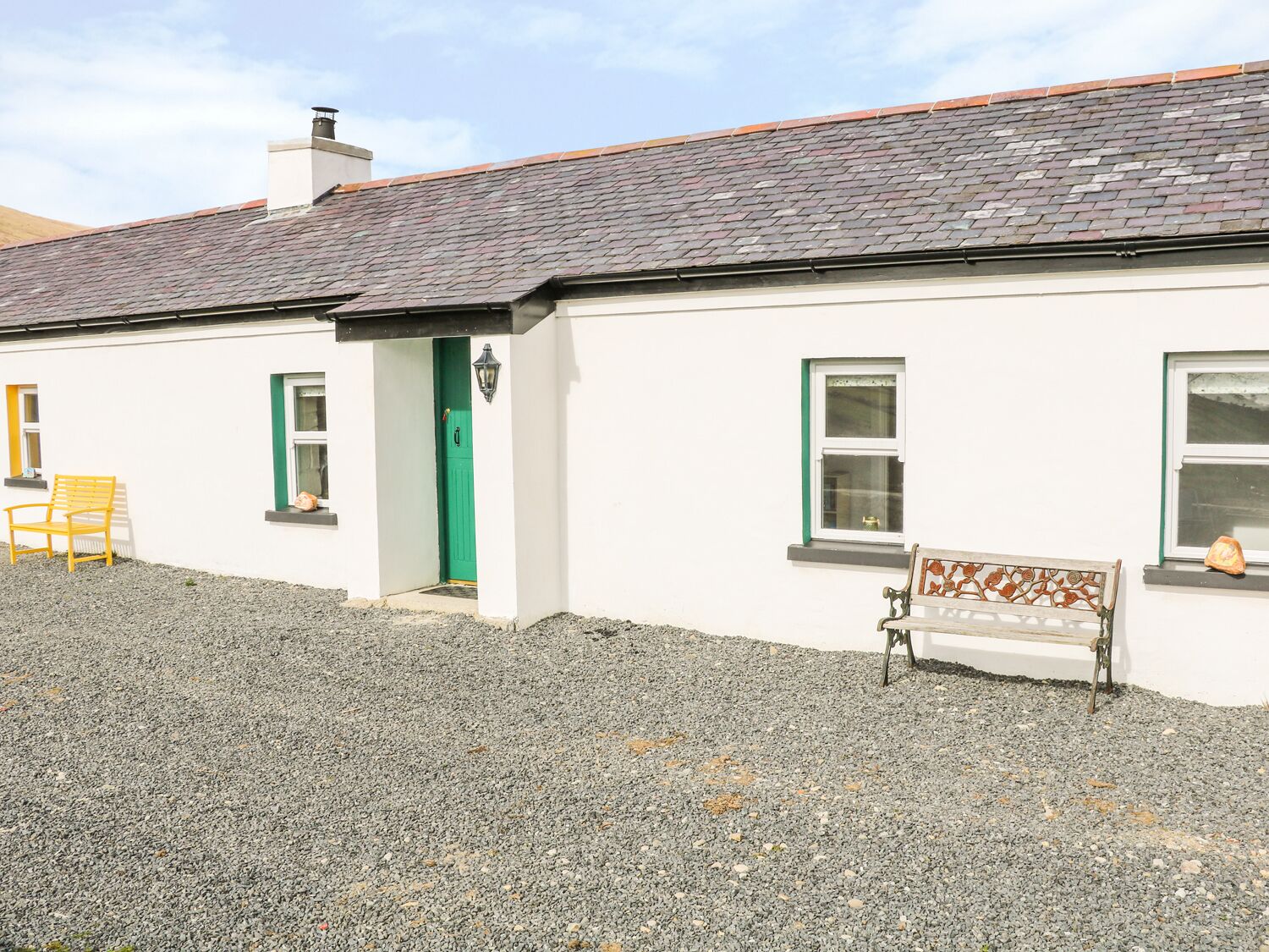 A white building with a grey tiled roof, a green door, and a bench outside.