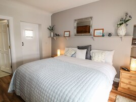 Un dormitorio con una cama grande, un aparador, una mesita de noche, un espejo y una estantería con objetos decorativos.