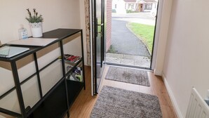 A hallway with a black metal desk, a potted plant, and a door leading outside. - Coneyville (Londonderry)