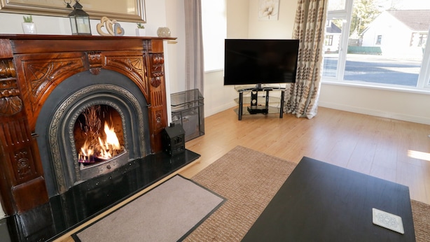 A living room with a fireplace, a television, and a large window with curtains. - Coneyville (Londonderry)