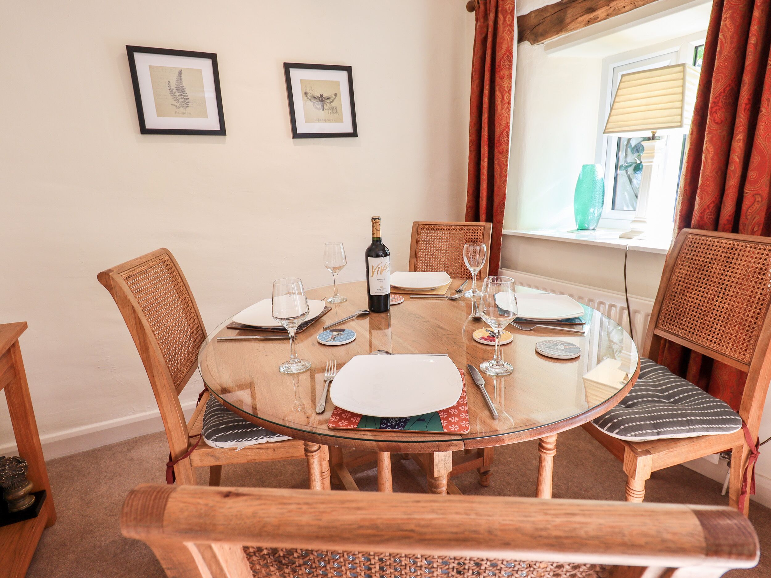 A dining table with chairs, a bottle of wine, and framed botanical prints on the wall.
