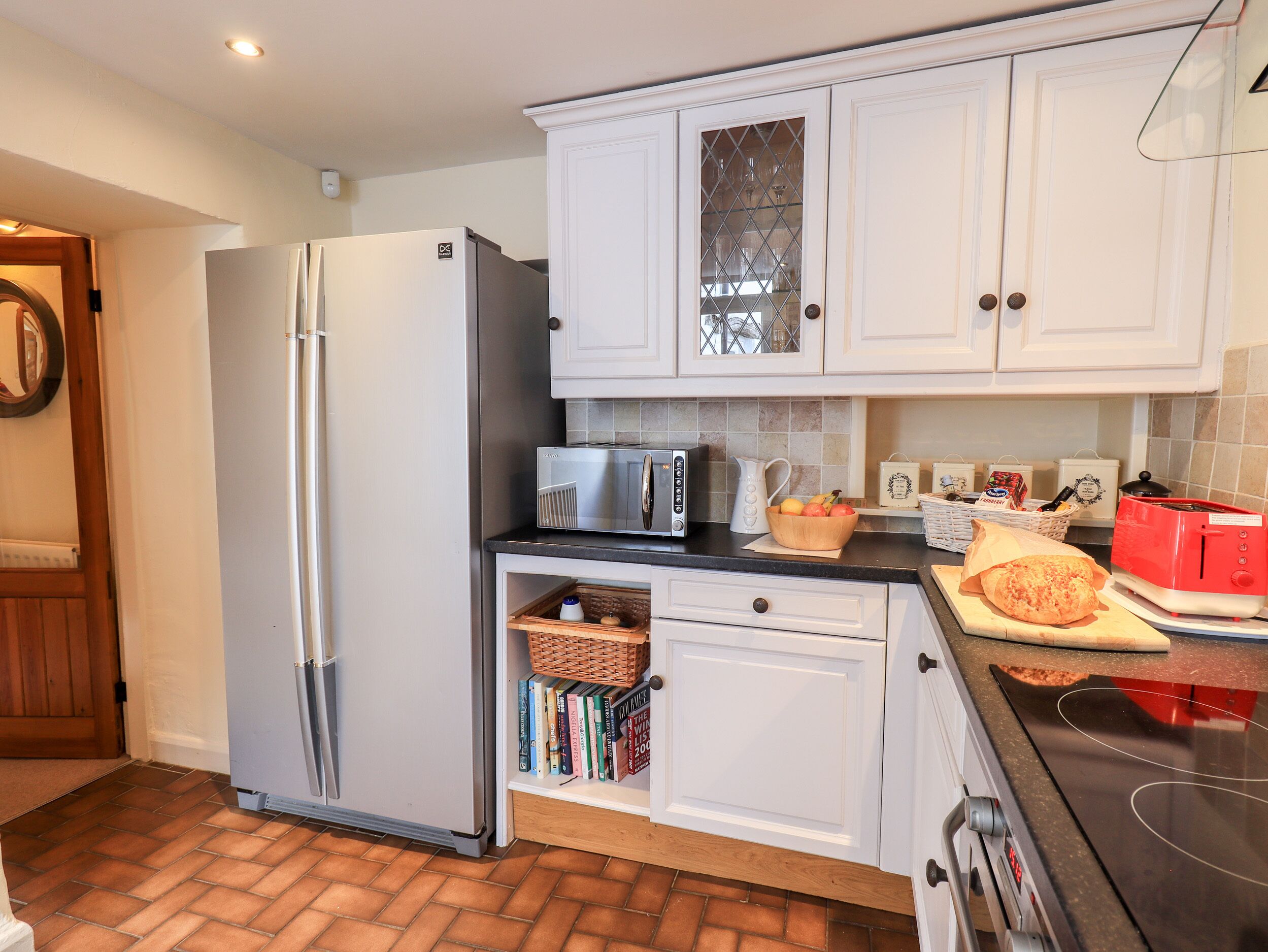 A modern kitchen with white cabinets, a stainless steel refrigerator, a microwave, and a red toaster.