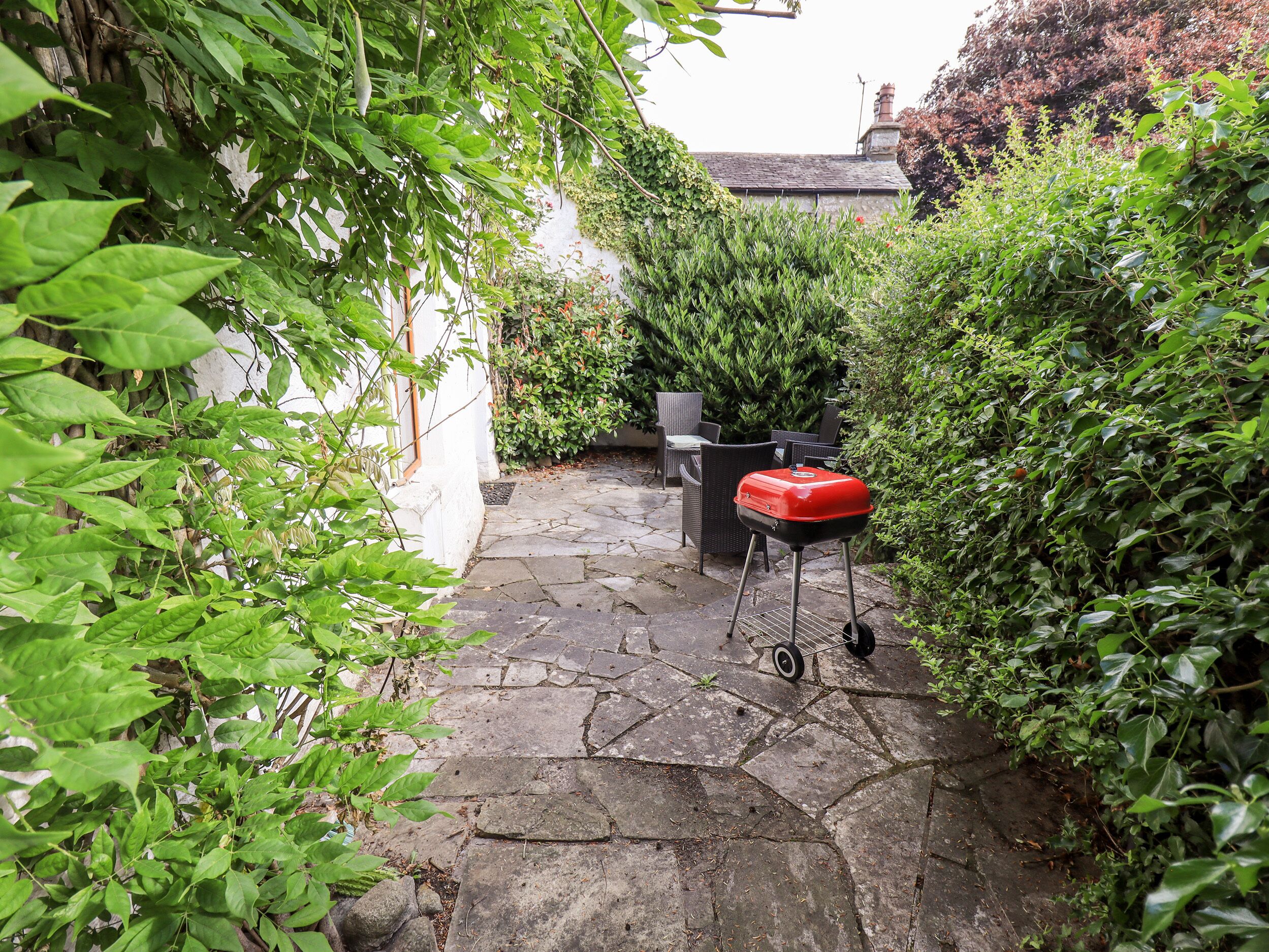 Une terrasse dallée de pierres, avec un barbecue rouge et une poubelle noire.
