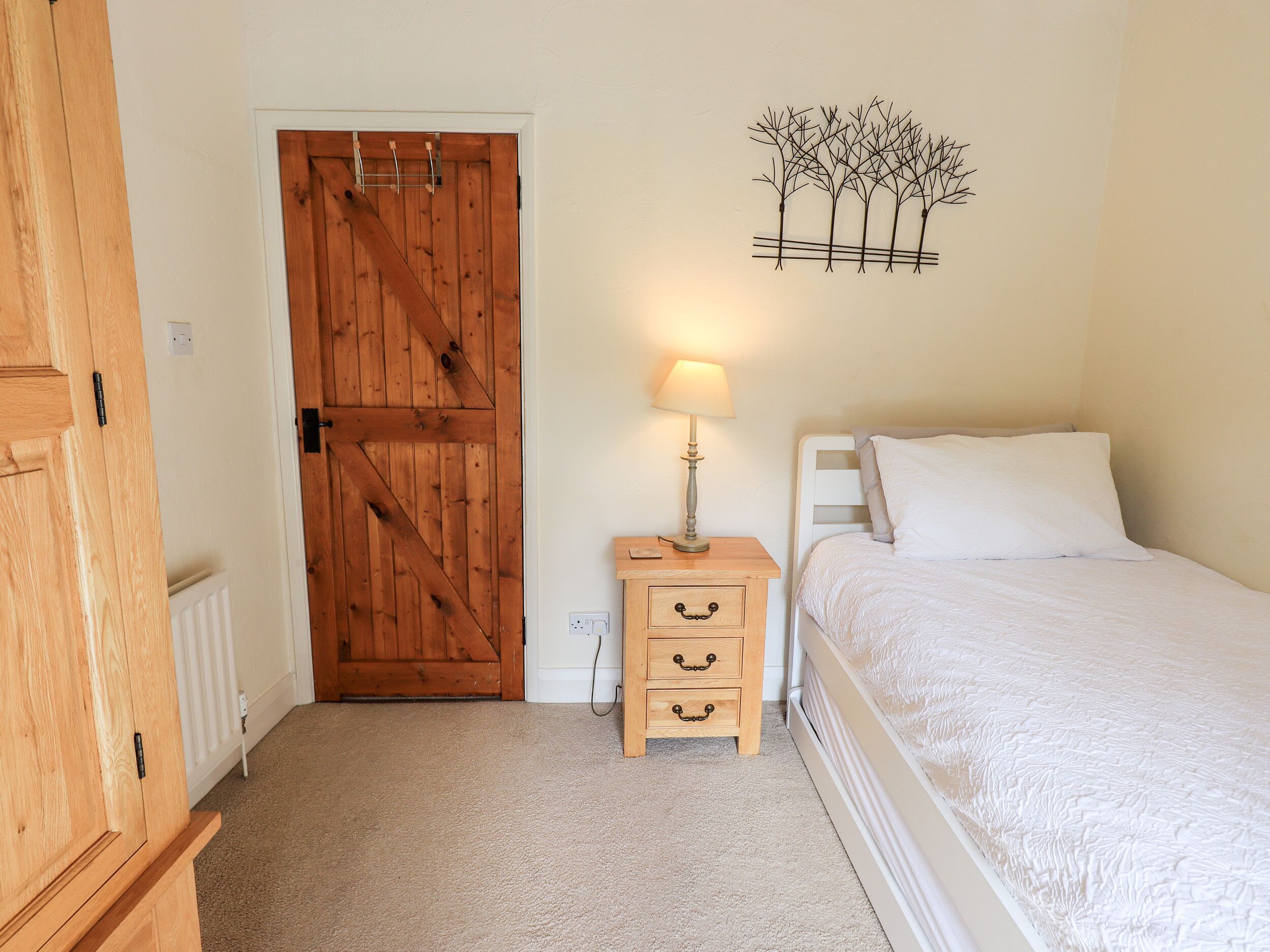 A bedroom with a wooden door, a bedside table with a lamp, and a bed with white bedding.