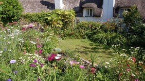 A traditional thatched-roof house with a well-maintained garden in front. - Appletree Cottage (Newton Abbot)