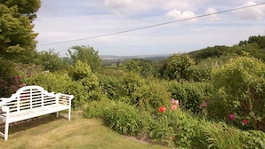A white bench in a garden with various plants and flowers, overlooking a landscape. - Appletree Cottage (Newton Abbot)