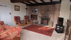 A cozy living room with a stone fireplace, patterned sofas, and wooden chairs. - Appletree Cottage (Newton Abbot)