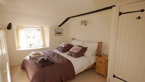 A bedroom with a bed, a nightstand, a window with curtains, a picture on the wall, and a door with a handle. - Appletree Cottage (Newton Abbot)