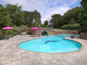 Relax by the serene pool surrounded by lush greenery and stone structures, featuring a curved pool with a dolphin-shaped cutout and two stone bridges.