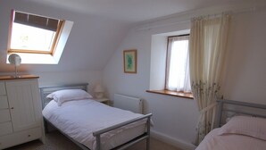A bedroom with a single bed, a small window with curtains, a radiator, and a white wardrobe. - The Old Cider Barn (Wells)