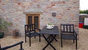 A stone building with a small patio area featuring a table and two chairs. - The Old Cider Barn (Wells)