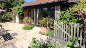 A house with a tiled roof, a wooden fence, and a garden with various plants and flowers.