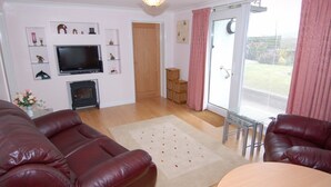 A living room with a fireplace, a television, and a sliding glass door to a balcony. - Garden View (Newton Abbot)