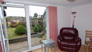 A living room with a sliding glass door leading to a garden, a red leather chair, a small table, and a lamp. - Garden View (Newton Abbot)
