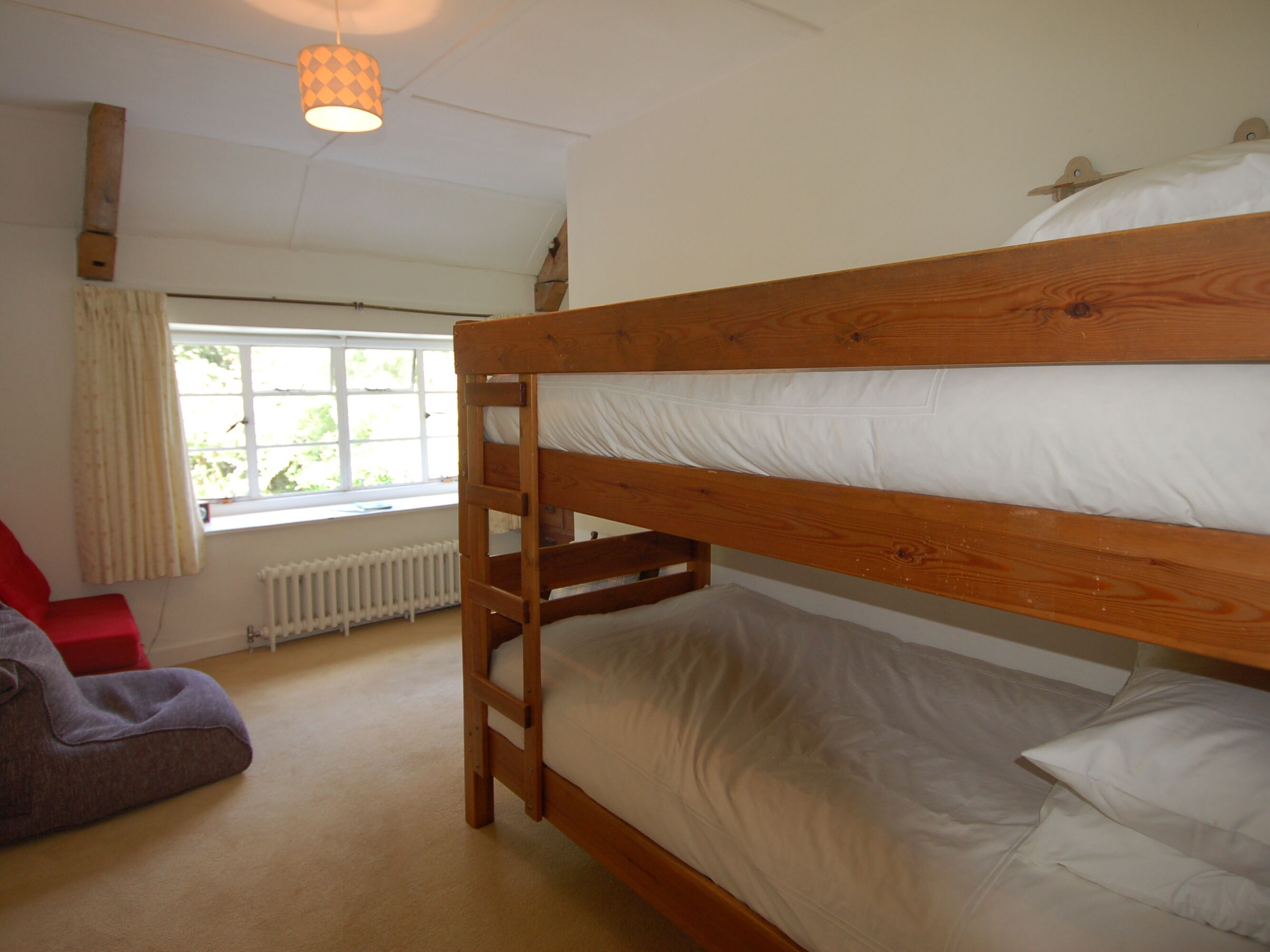 Een slaapkamer met een stapelbed, raam, radiator en hanglamp.