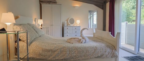 A bedroom with a bed, bedside lamps, a wardrobe, a dresser, a mirror, and a window with curtains.