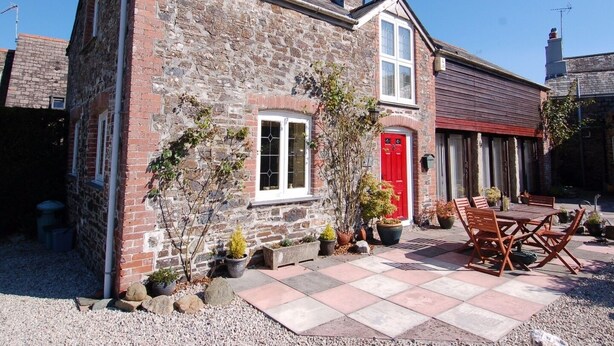 A stone house with a red door, a small garden with potted plants, and outdoor seating. - Jacobs Barn (Lifton)