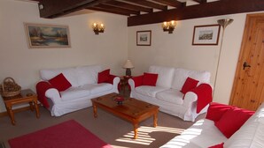 A living room with two white sofas, red cushions, a wooden coffee table, and a red rug. There are wall-mounted lamps and framed pictures on the walls. - Jacobs Barn (Lifton)