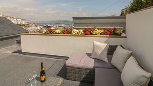 Une terrasse sur le toit avec un canapé en osier, une bouteille de champagne et un parterre de fleurs.