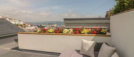 A rooftop terrace with a wicker sofa, a bottle of champagne, and a flower bed.