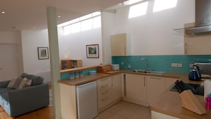 A compact kitchen with a dishwasher, a sink, and a toaster. There is a small dining area with a table and a chair. - Orchard Retreat (Sidmouth)