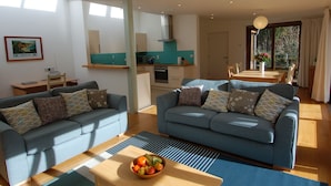 A modern living room with two sofas, a dining table, and a kitchen area. - Orchard Retreat (Sidmouth)