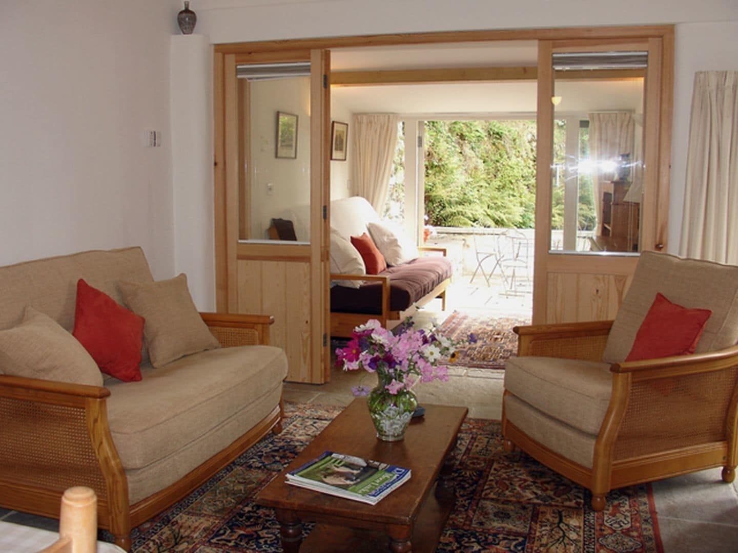 A cozy living room with a sofa, armchairs, a coffee table, and a view of the garden through a sliding door.