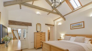 A bedroom with a wooden bed, a dresser, a mirror, and a painting on the wall. - Burham Barn (Yelverton)