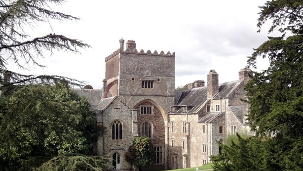 A historic stone building with a prominent tower, arched windows, and a well-maintained lawn. - Burham Barn (Yelverton)