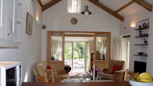 A cozy living room with a wooden ceiling, a dining area with a table and chairs, and a kitchen area with a microwave. - Burham Barn (Yelverton)