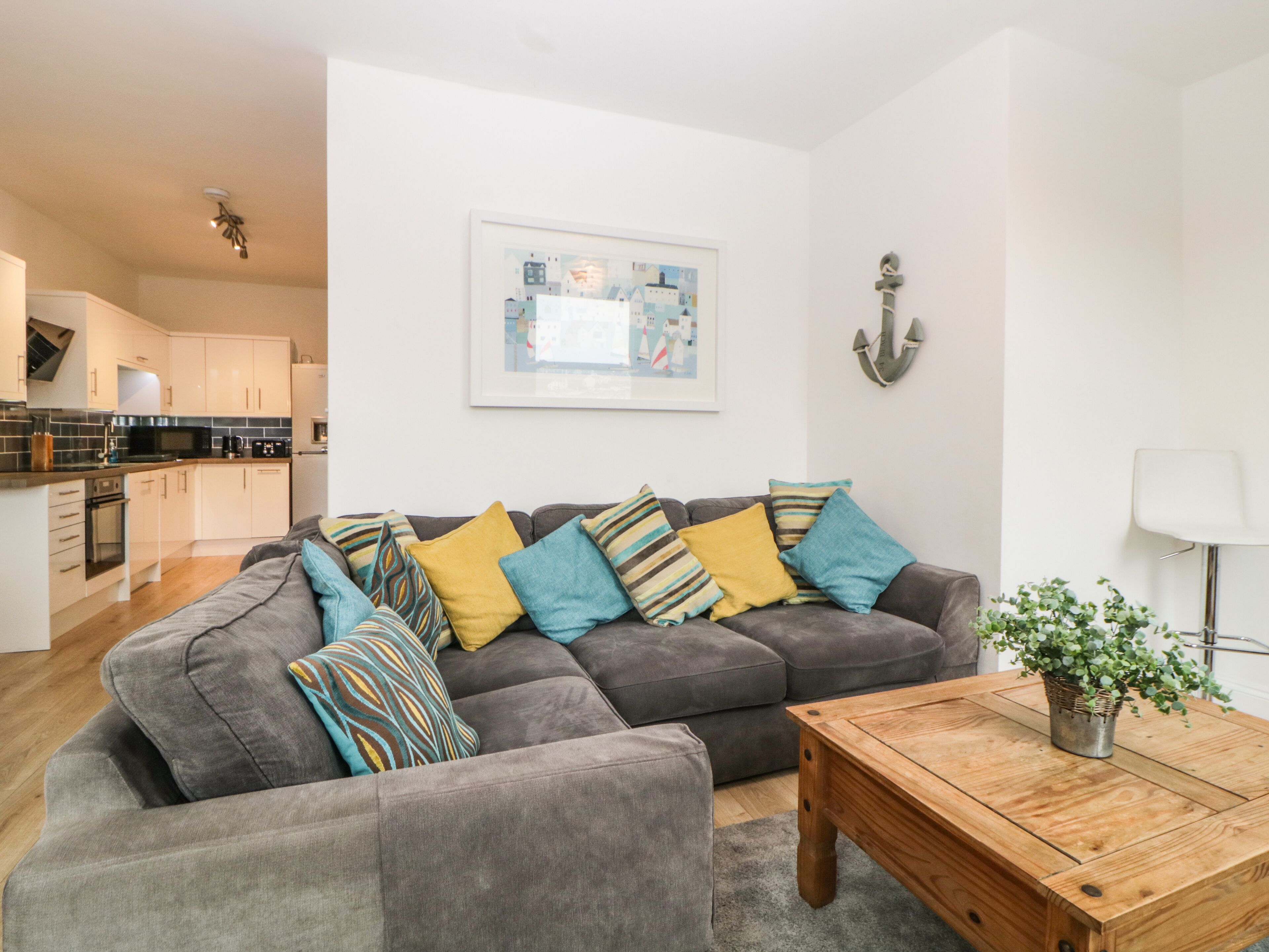 A modern living room with a grey sofa, colorful cushions, a wooden coffee table, and a framed picture on the wall.