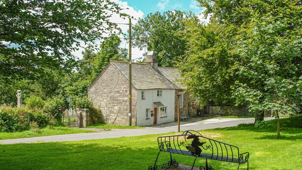 A stone house with a white exterior, a small porch, and a metal bench in front.