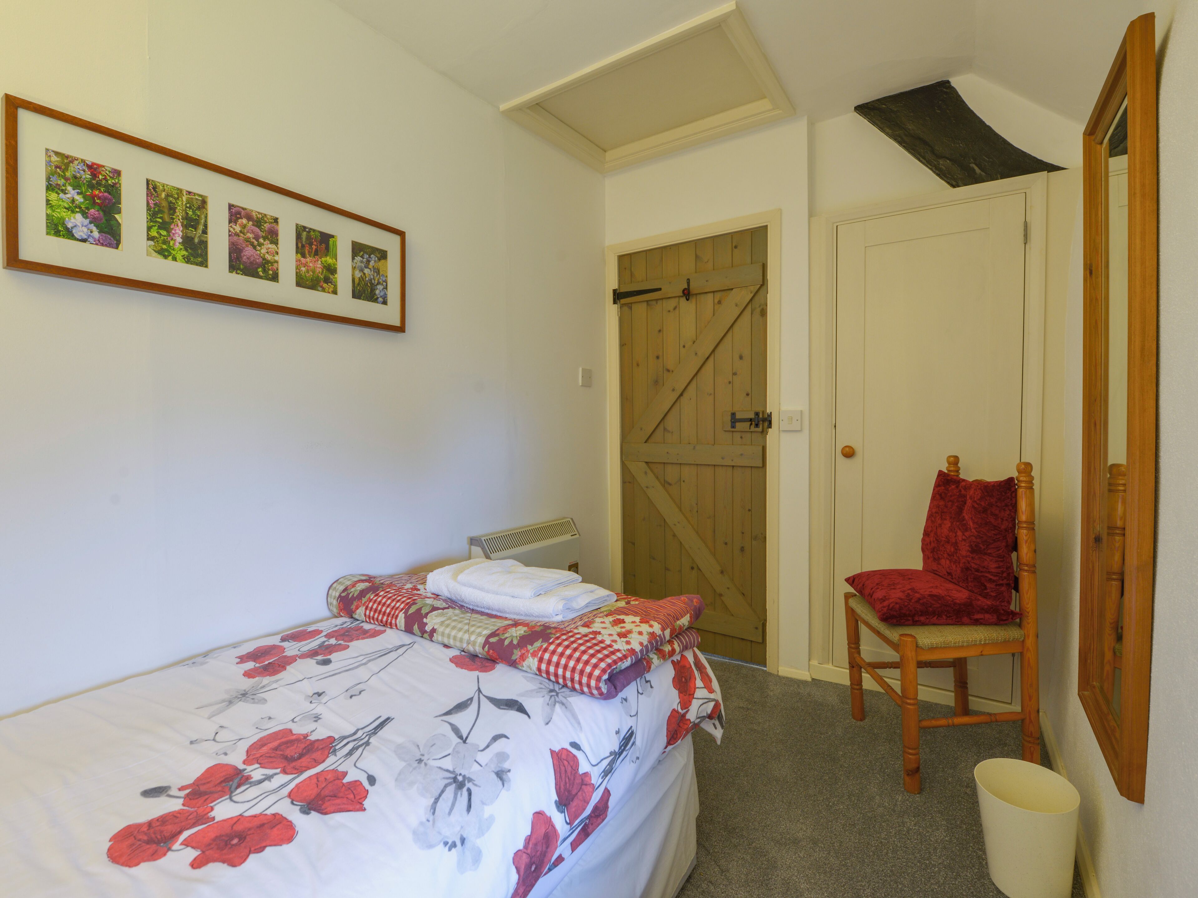 A bedroom with a bed, a chair, a wooden door, and a framed picture on the wall.