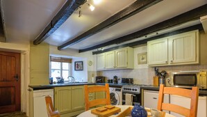 A kitchen with a sink, stove, microwave, and wooden chairs around a table with a tray of teapots.
