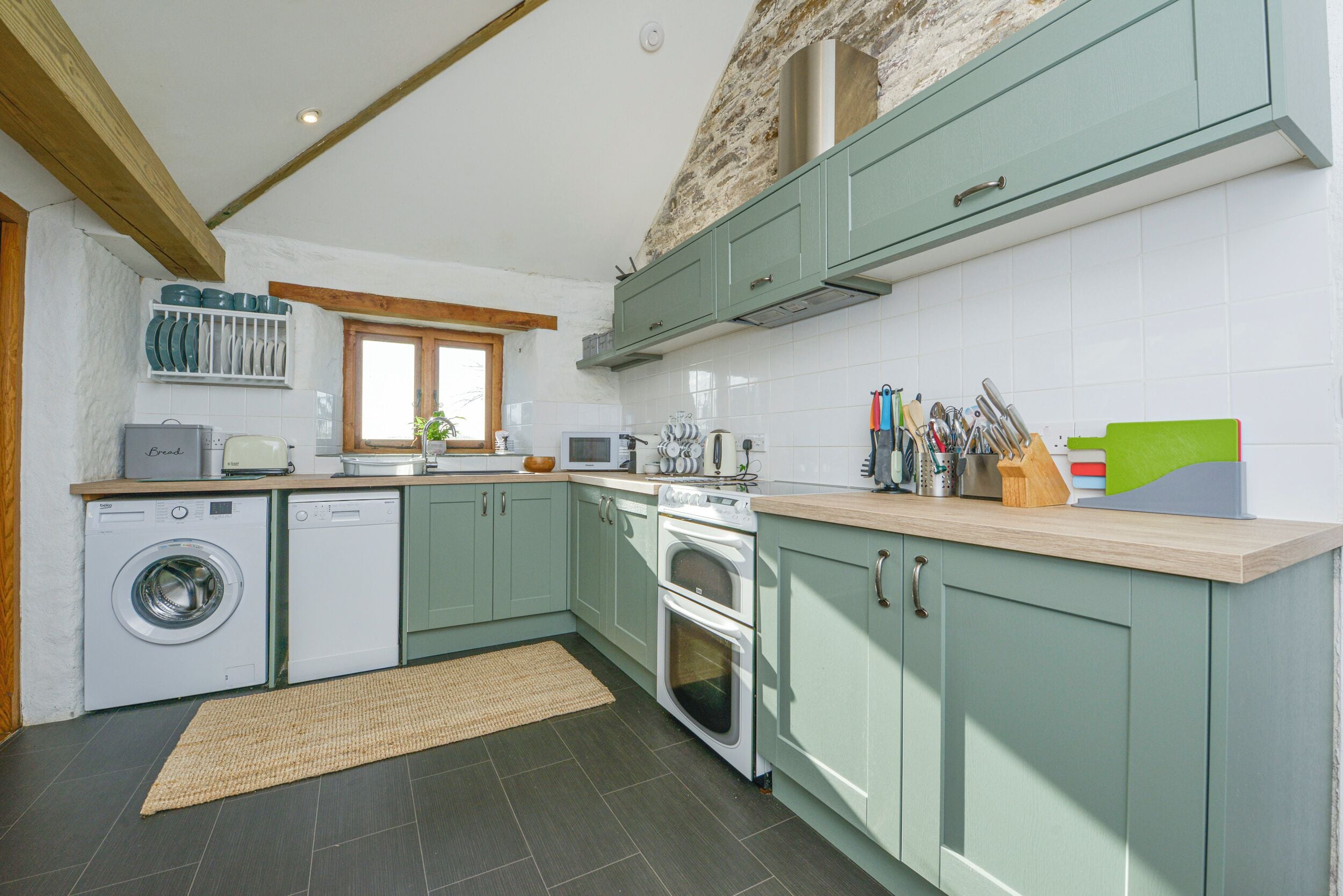 A kitchen with green cabinets, a washing machine, a stove, and a window.