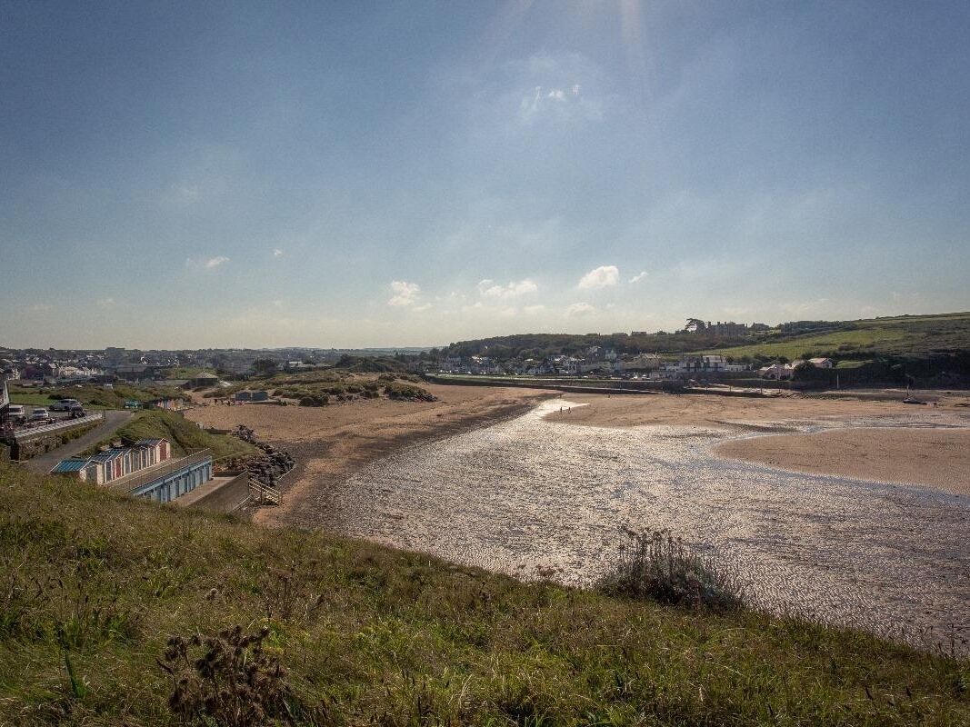 A coastal landscape with a beach, a small building with a blue roof, and a distant town.