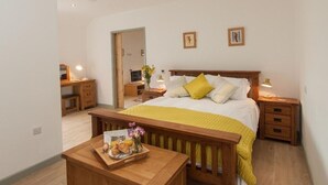 Un dormitorio con cama, mesitas de noche, un banco de madera y una pequeña mesa con una bandeja de comida.