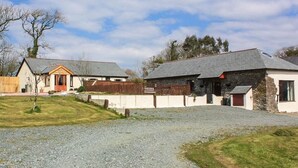 Una propiedad rural con camino de grava, cerca de madera y dos edificios con fachada de piedra y madera.