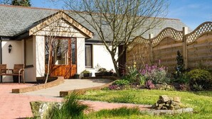 Una casa con cerca de madera, un jardín con flores y un camino de ladrillo.