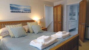 Una cama bien hecha con almohadas, una lámpara de noche y toallas dobladas sobre un marco de madera.