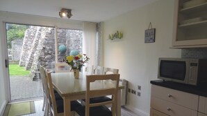 Un área de comedor con una mesa, sillas, un florero y vistas a un muro de piedra y follaje exterior.