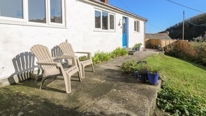 A white house with a blue door, two plastic Adirondack chairs, and potted plants in the yard. - Cockle Island Cottage (Helston)