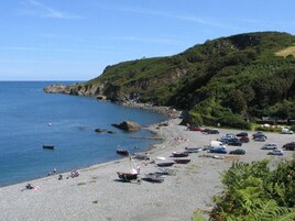 A coastal area with a pebble beach, boats, and parked cars.
