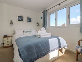 A bedroom with a bed, a nightstand, a chair, and a window with curtains.