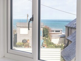 Vista desde una ventana de una zona residencial, con cielo despejado, una masa de agua y casas con techos y cercas visibles.