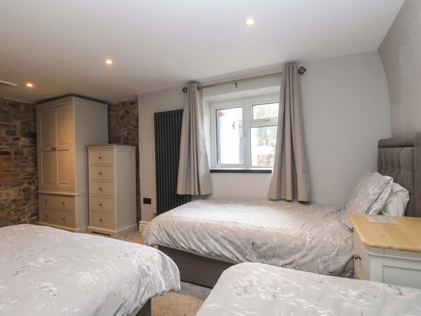 A bedroom with two beds, a wardrobe, a window with curtains, and a stone wall.