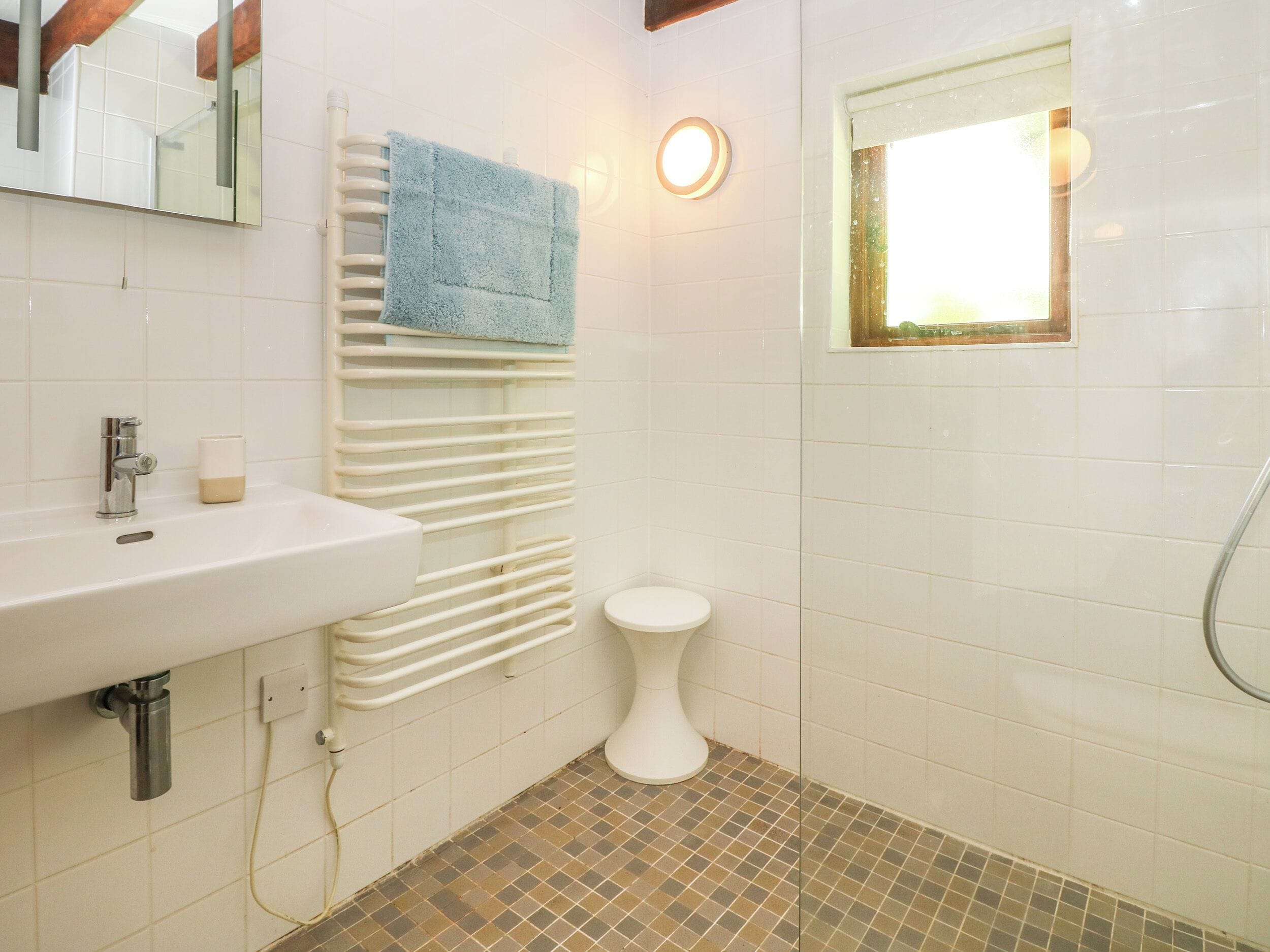 A bathroom with a white sink, a toilet, a towel rack with a blue towel, a mirror, and a window with a light fixture.