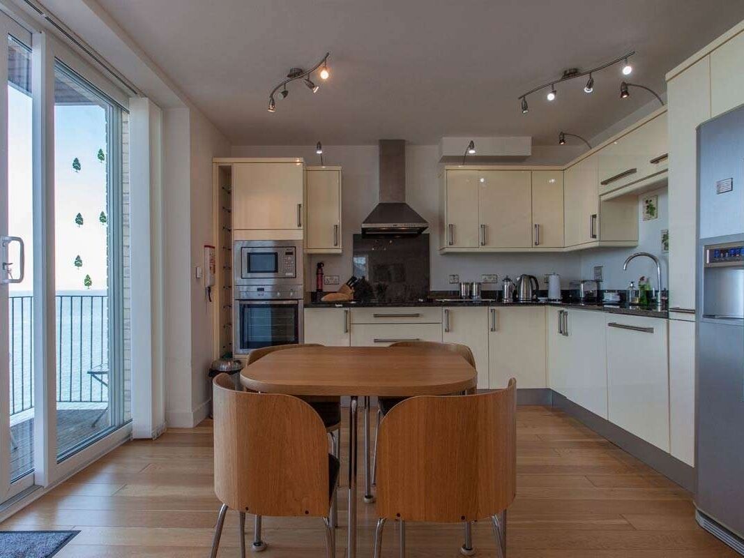 A modern kitchen with a dining table and chairs, built-in appliances, and a large window.