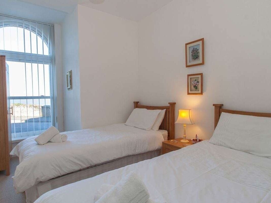 Habitación de hotel con dos camas, una ventana con persianas y una mesita de noche con lámpara.