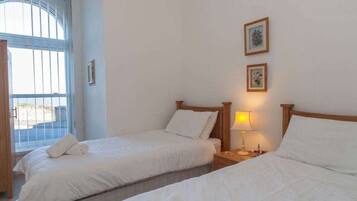Habitación de hotel con dos camas, una ventana con persianas y una mesita de noche con lámpara.